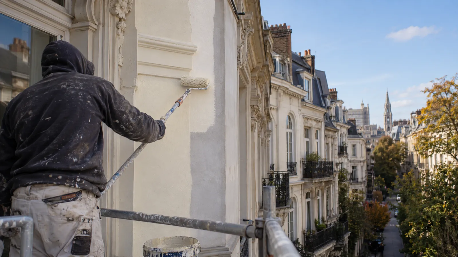 Peintre appliquant la peinture de finition au rouleau sur la façade d'une maison de maître à Bruxelles