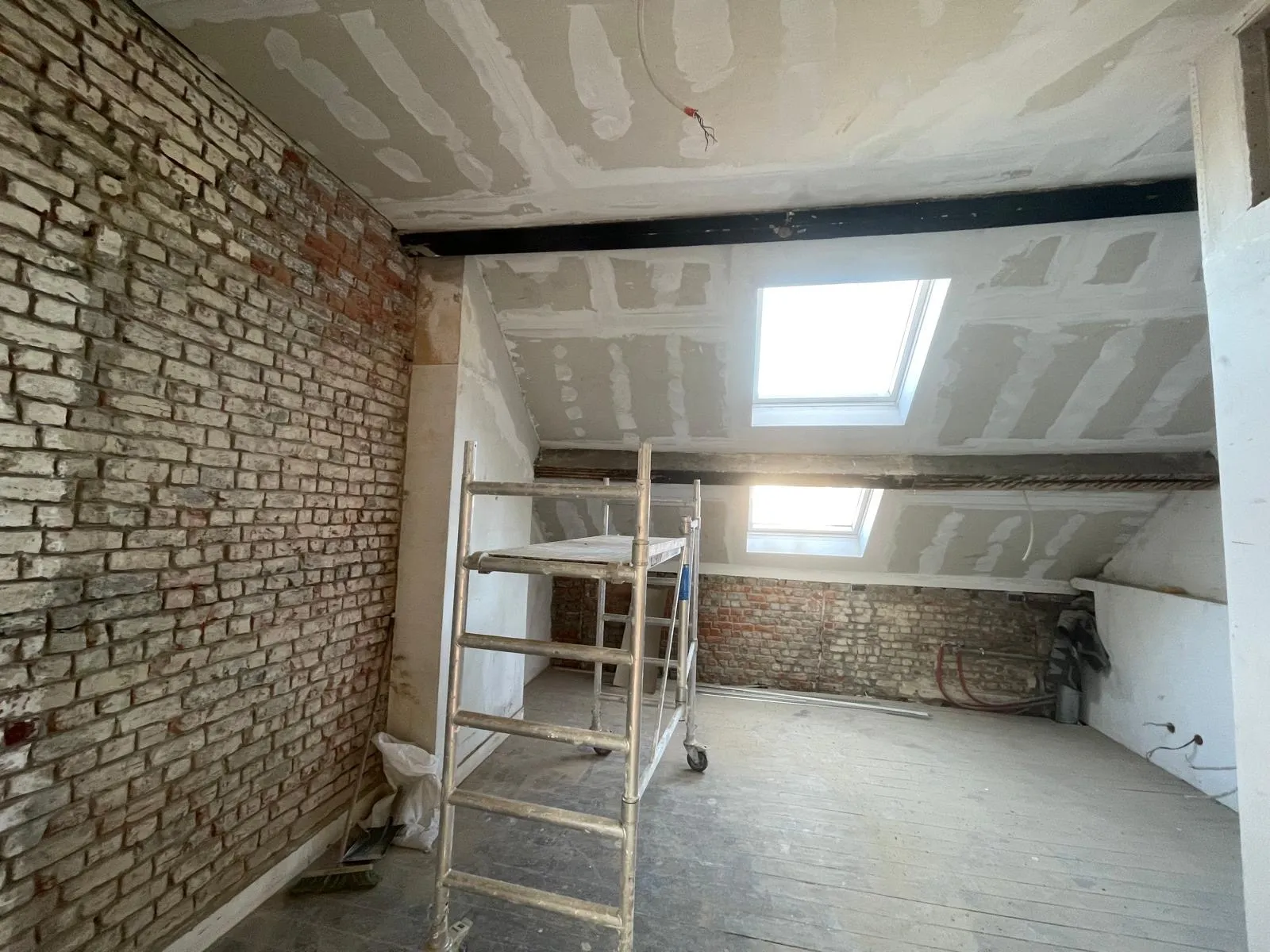 Avant travaux : combles en cours de plafonnage, brique nue, bandes de placo au plafond, échafaudage sous les velux