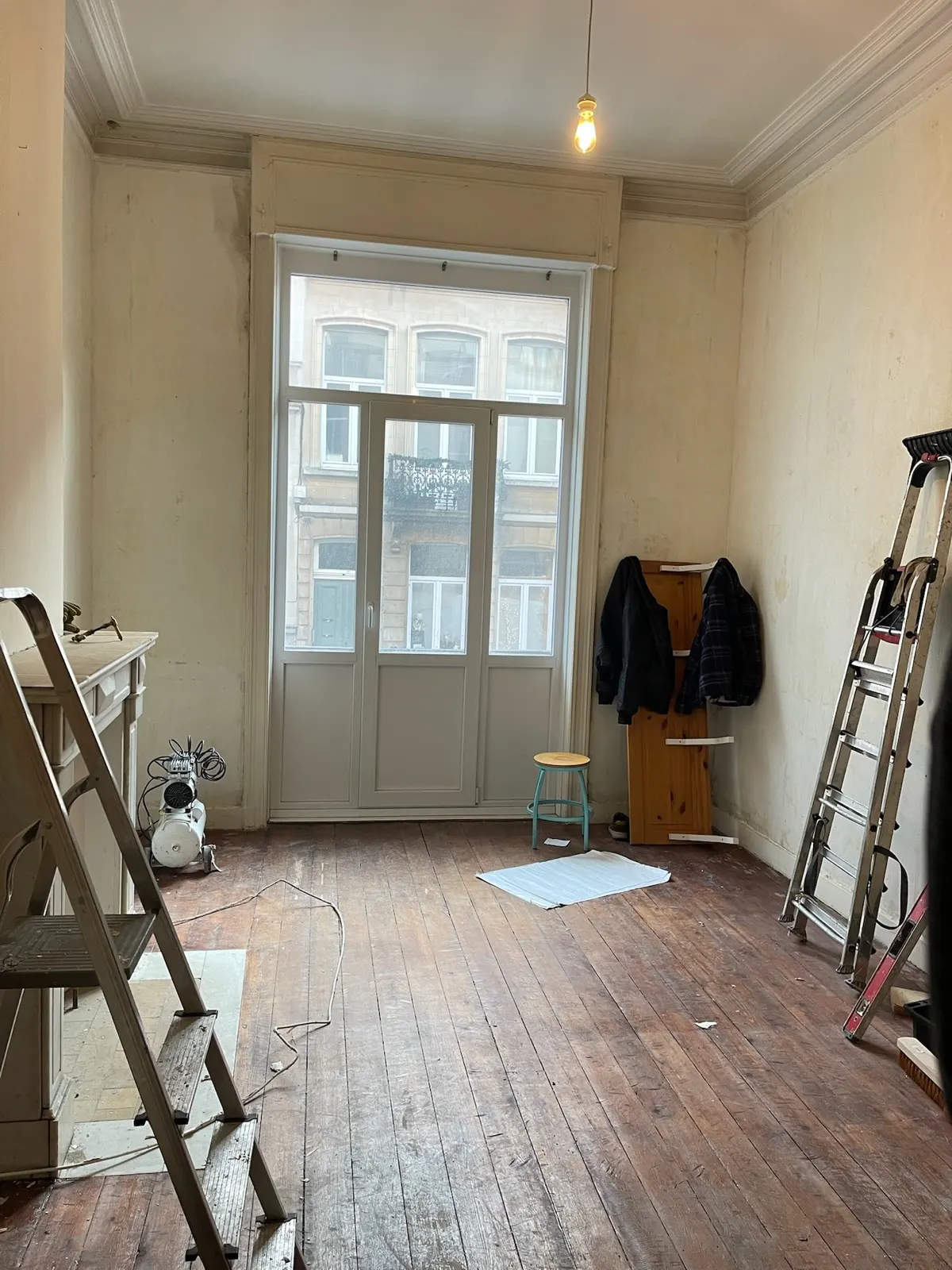 Avant travaux : salon d'une maison bruxelloise aux murs défraîchis, cheminée d'origine et plancher brut