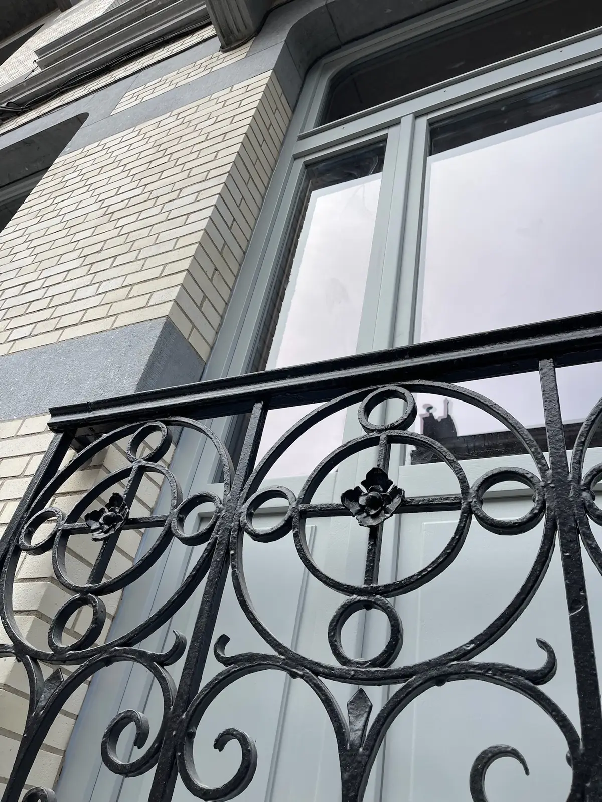 Détail d'une ferronnerie de balcon restaurée devant un châssis gris