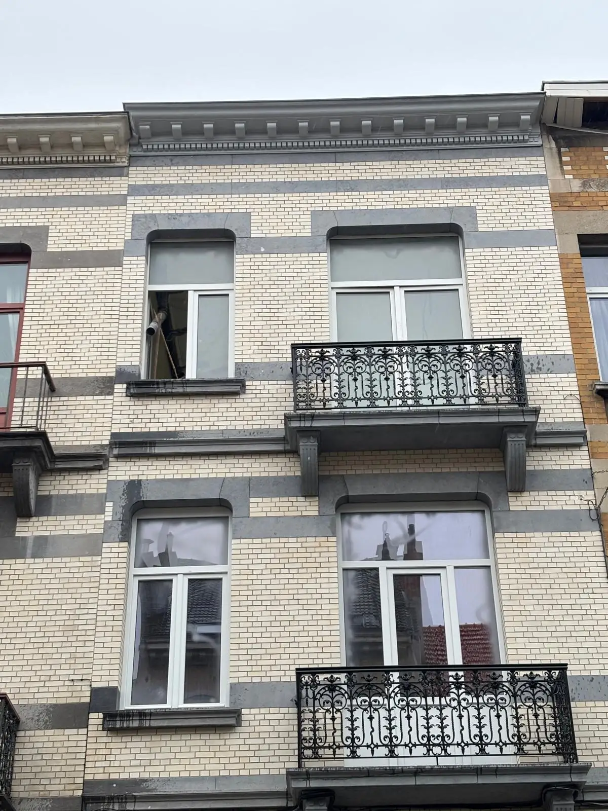 Façade de maison de maître en briques claires, bandeaux de pierre bleue et balcons en fer forgé
