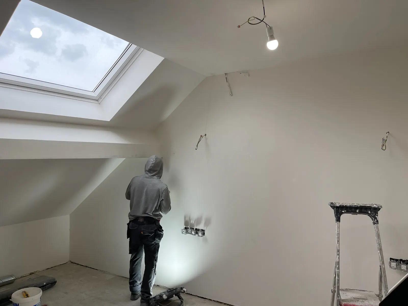 Peintre appliquant la finition sur un mur sous rampant, velux ouvert sur le ciel