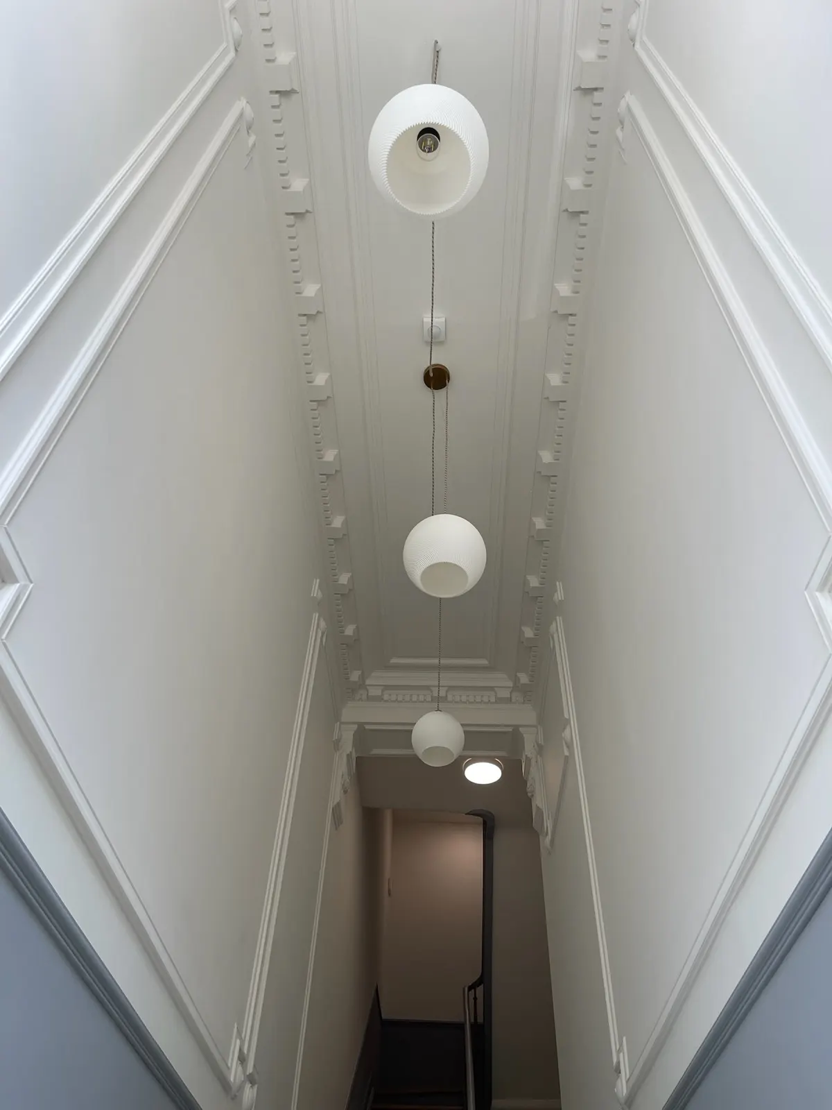 Cage d'escalier de maison de maître repeinte en blanc, corniches à denticules et suspensions opalines