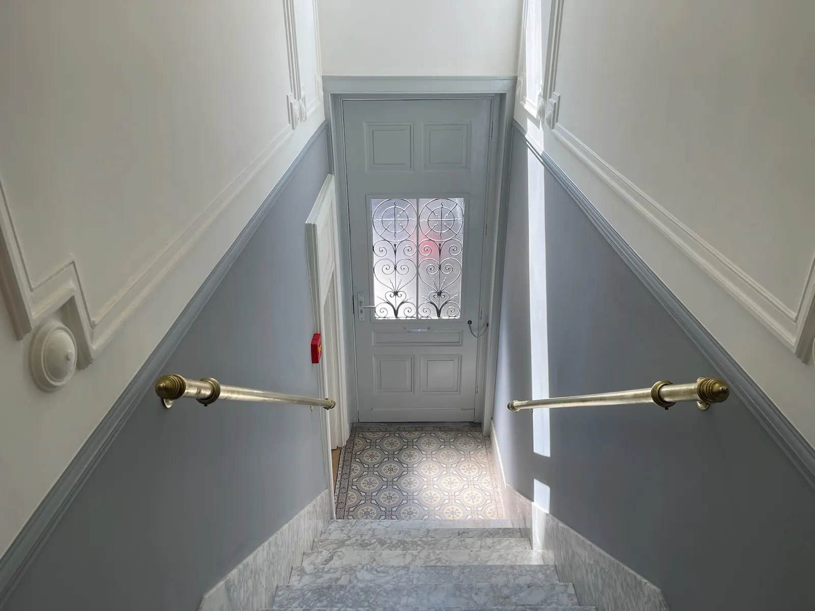 Hall d'entrée bruxellois : soubassement gris, murs blancs et carreaux de ciment d'origine conservés