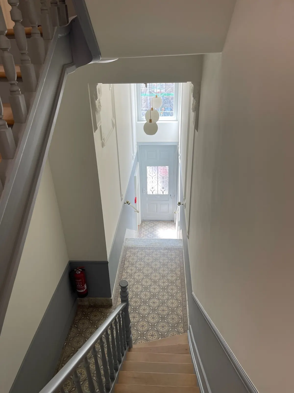Vue plongeante sur une cage d'escalier repeinte, carreaux de ciment anciens préservés