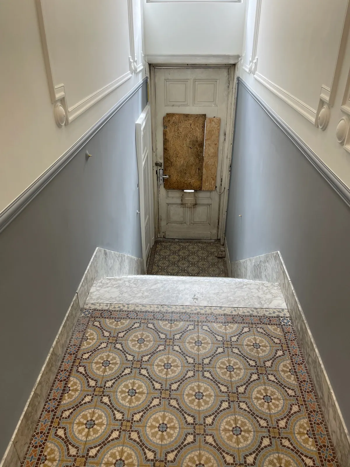 Escalier en marbre et hall à soubassement gris, porte d'entrée en cours de rénovation
