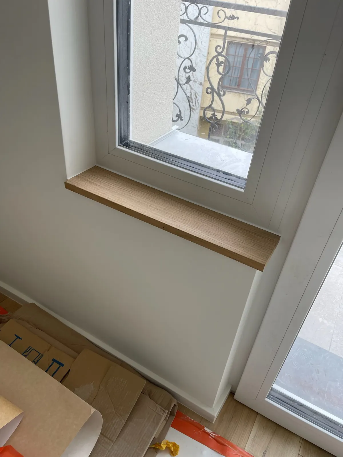 Encadrement de fenêtre repeint en blanc avec tablette bois, ferronnerie visible dehors