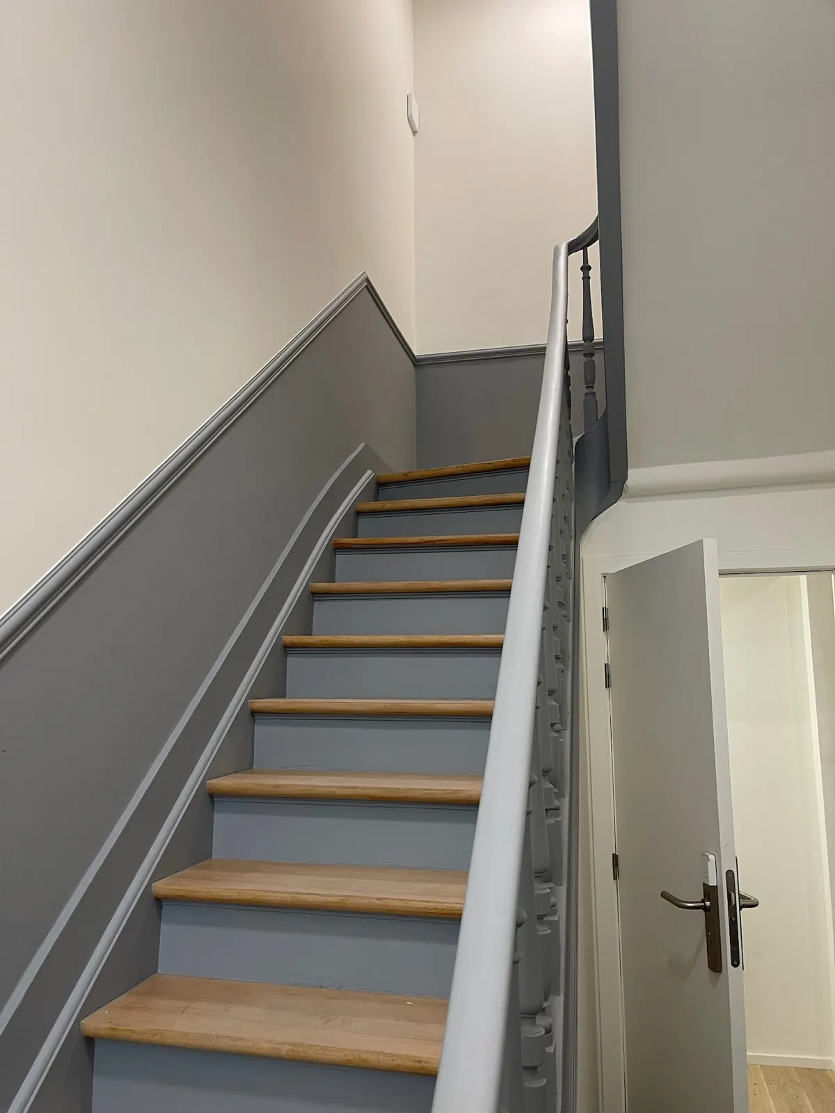 Escalier intérieur gris et bois avec soubassement mouluré courant le long de la montée
