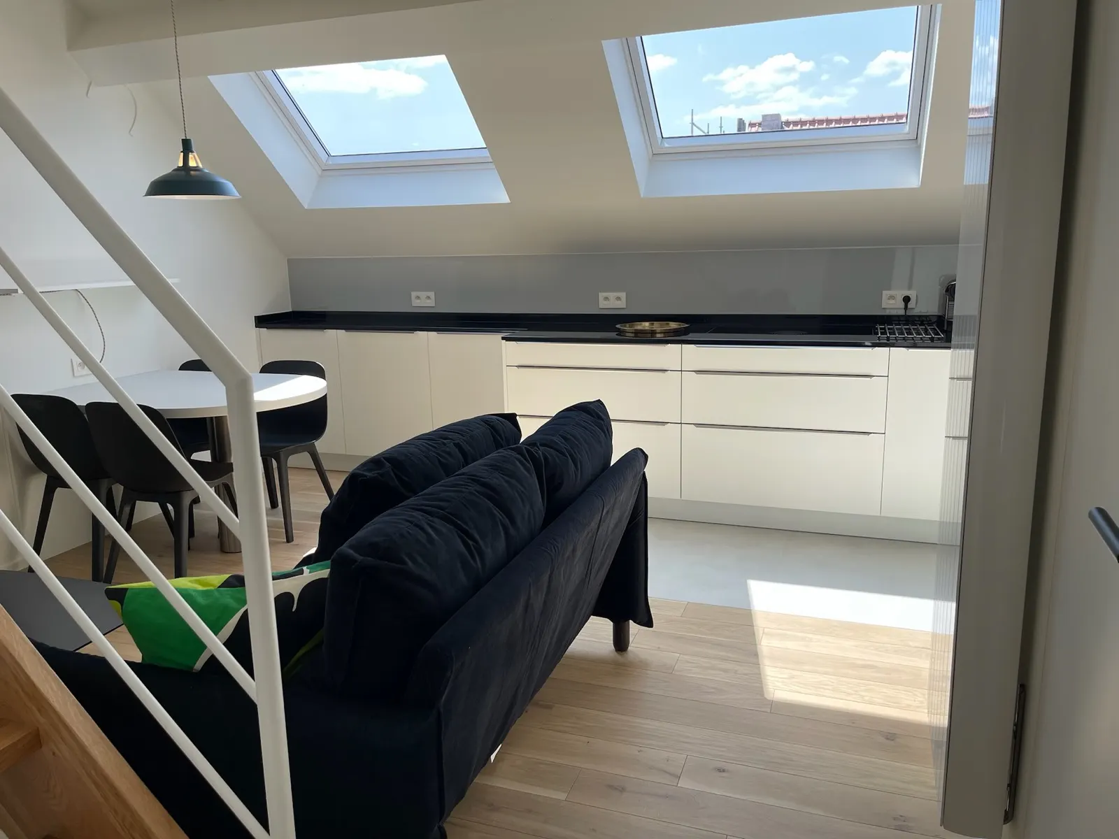 Pièce de vie sous combles éclairée par deux velux, cuisine blanche et plan noir