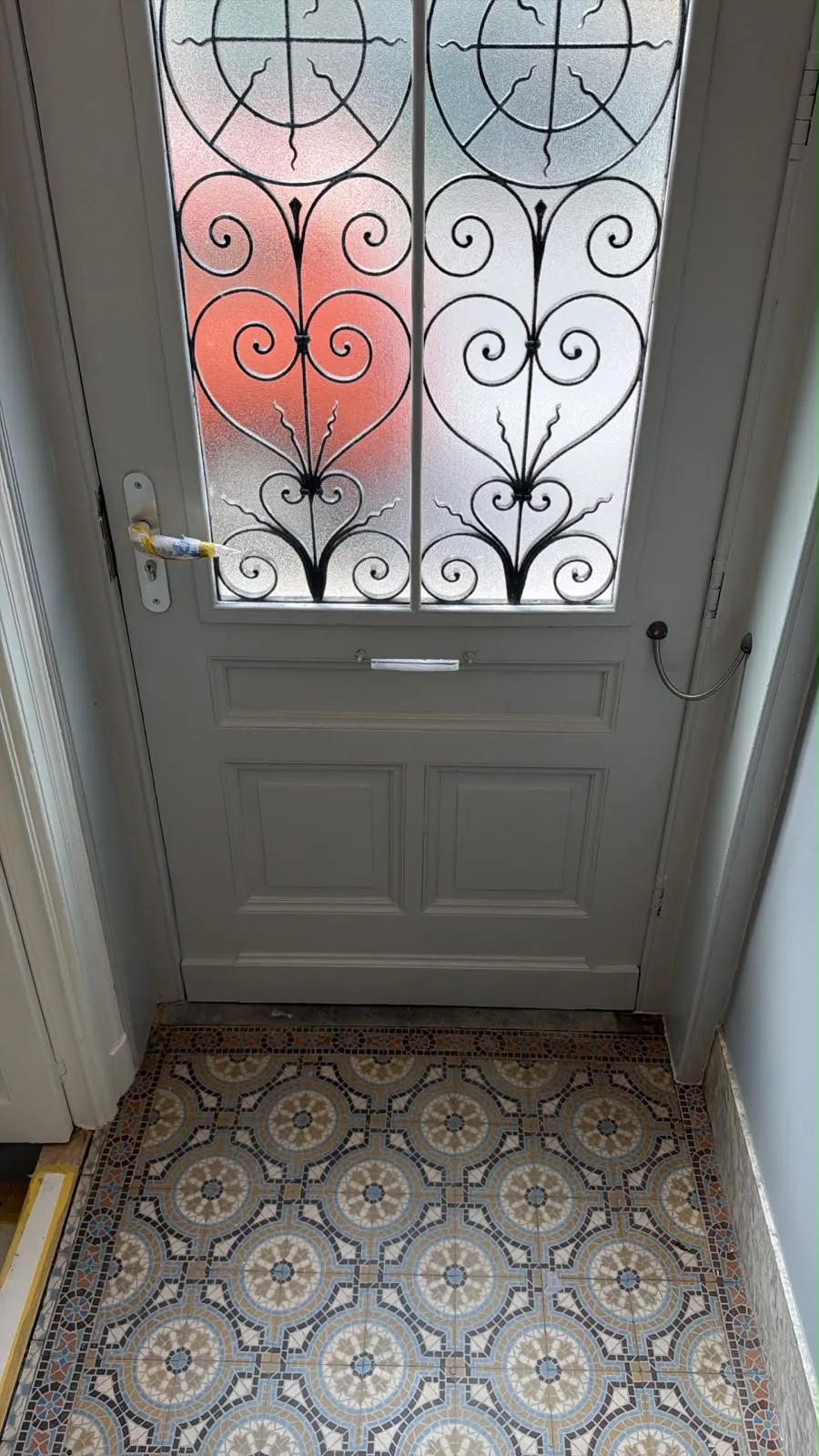 Porte d'entrée repeinte en gris, vitrail d'origine et sol en carreaux de ciment