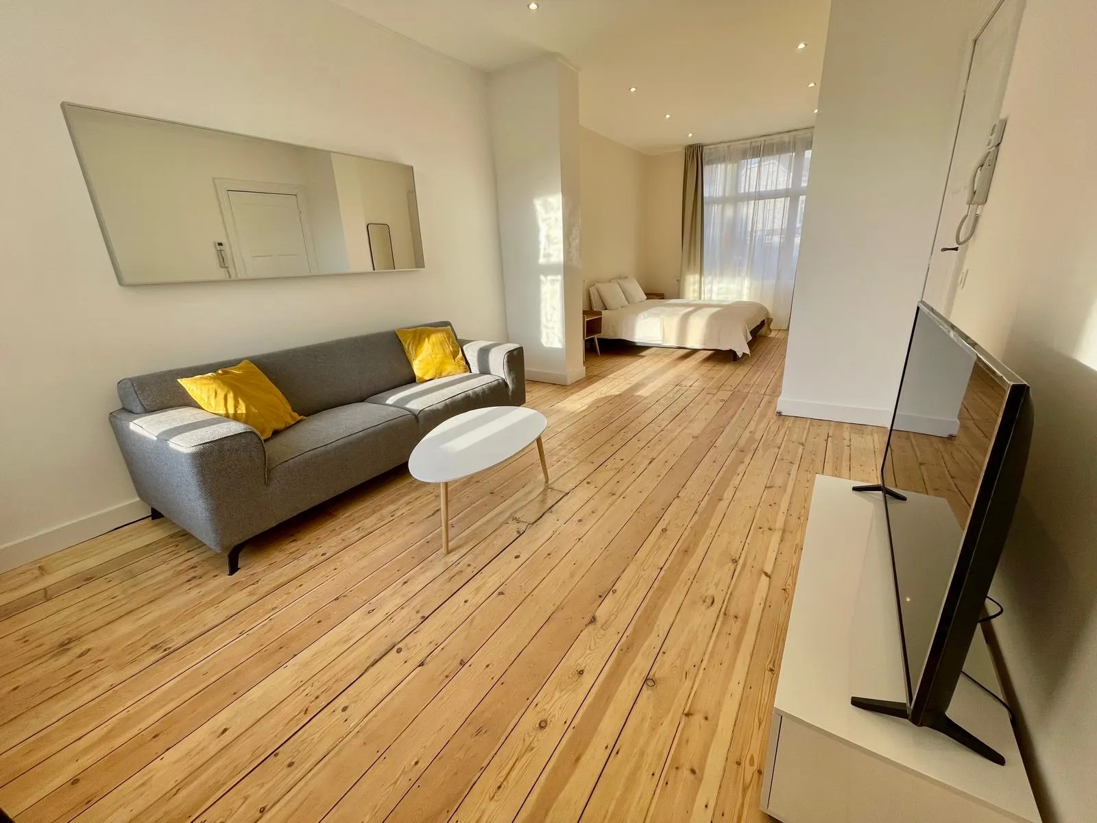 Studio traversant repeint en blanc, plancher en pin poncé, coin nuit près de la fenêtre